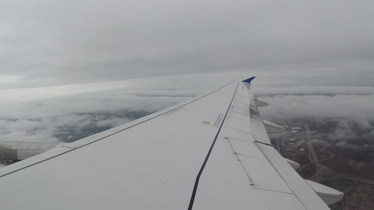 Airplane wing and blue wingtip above clouds and roads.