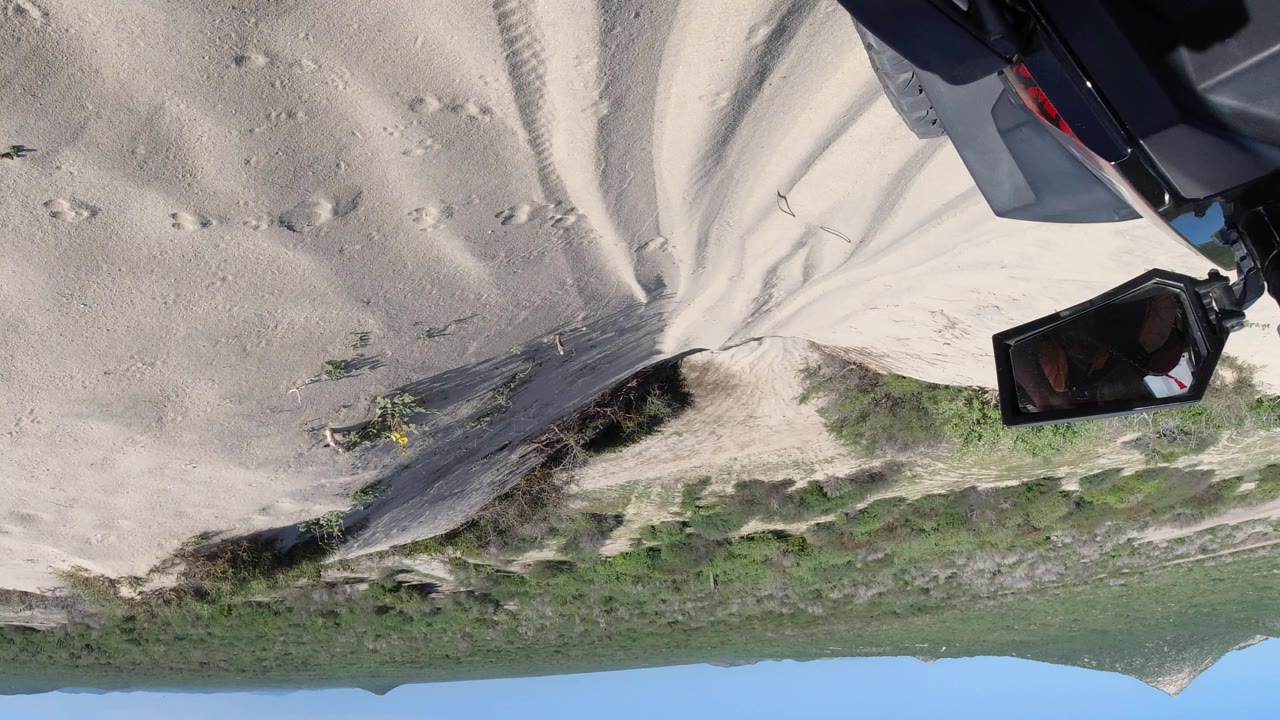 Upside-down sandy terrain, green brush, distant ridge, and blue sky.