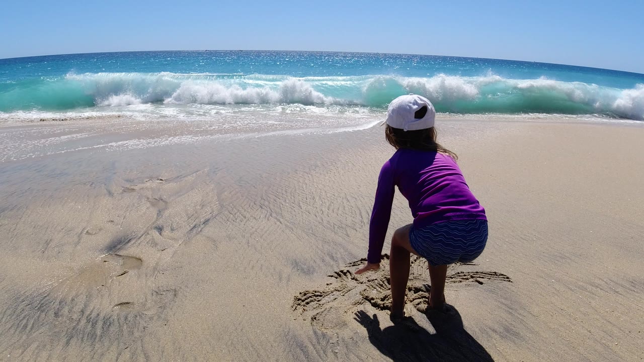 Child crouching on sand near breaking surf.