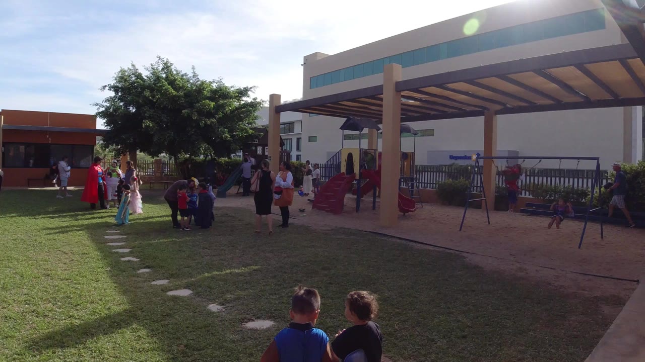 Children and adults gather in a grassy courtyard near playground equipment.