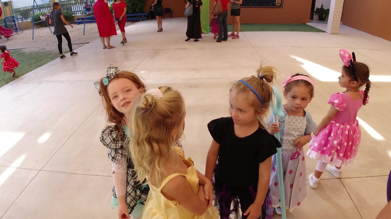 Young girls in dress-up outfits gather on a patio.