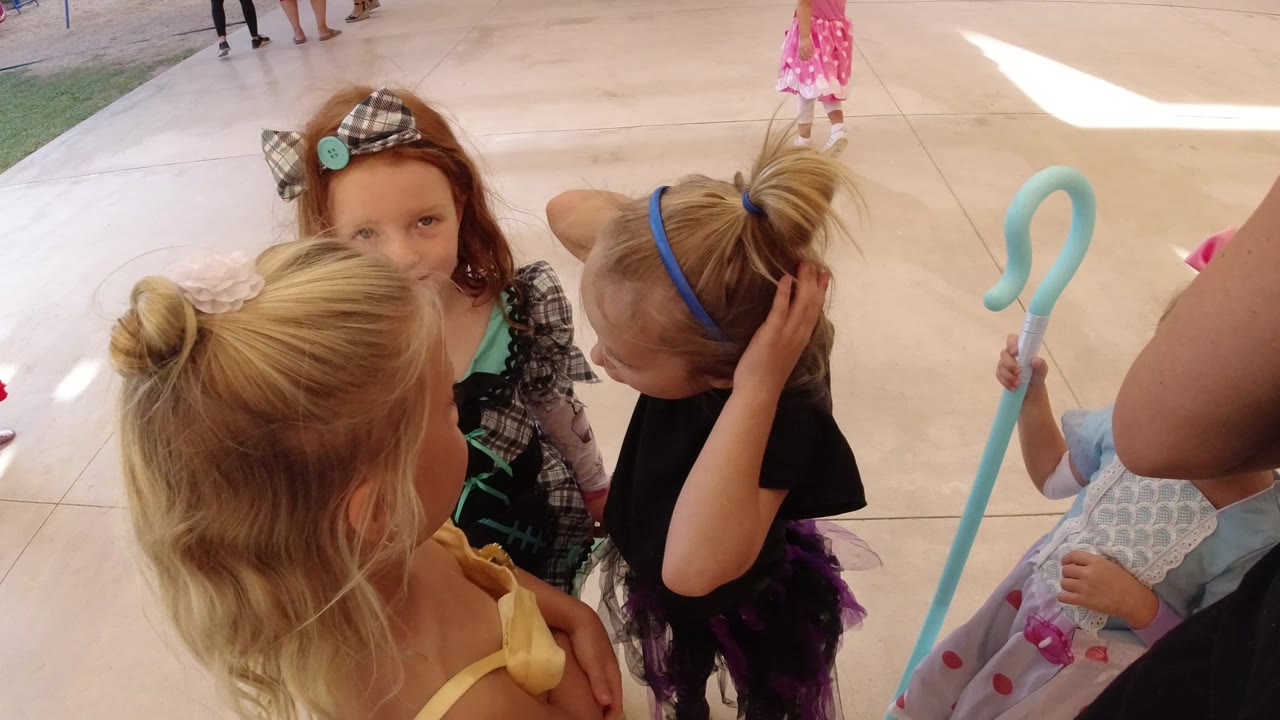 A close overhead view shows costumed girls on the Los Cabos patio, with one child looking toward the camera and another touching her hair.