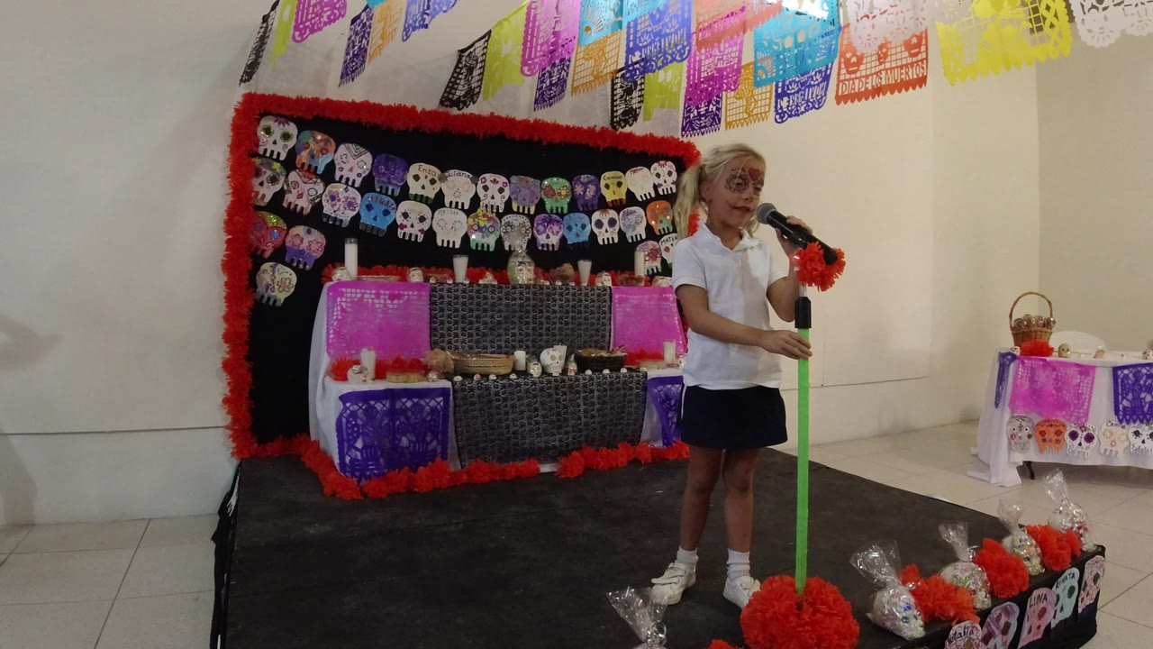 Young girl at a microphone in front of a decorated classroom display.