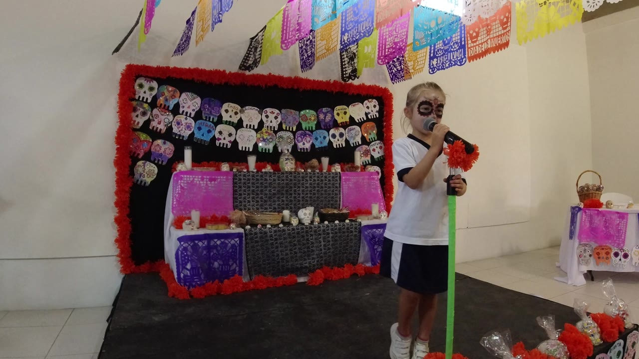 Young girl singing into a microphone beside a decorated skull backdrop.