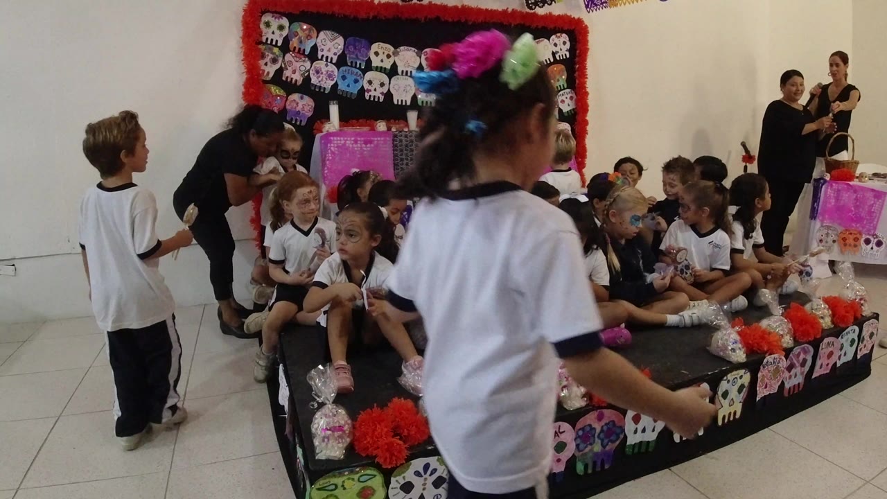 A child with colorful hair accessories passes close to the camera as classmates sit on the decorated school platform in Los Cabos, Mexico.
