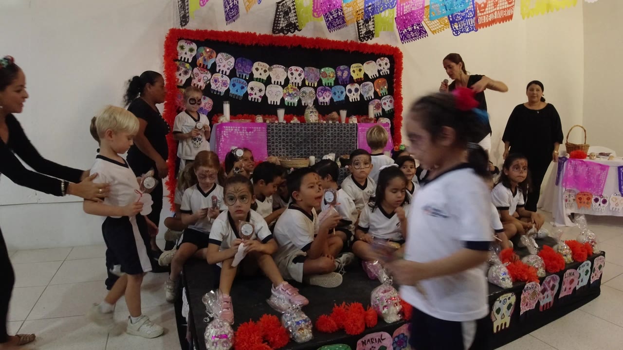 In Los Cabos, Mexico, a child passes close to the camera while seated children and adults continue arranging a group photo behind her.