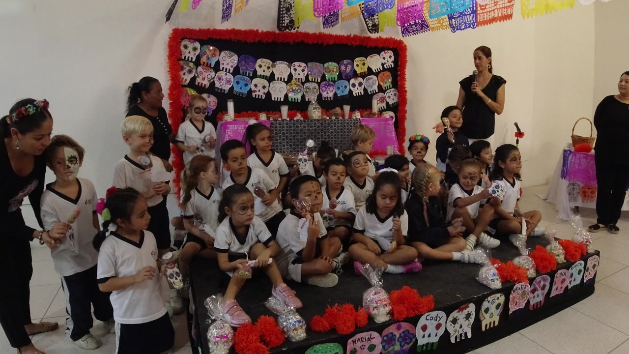 Schoolchildren and adults gathered around a Day of the Dead display.