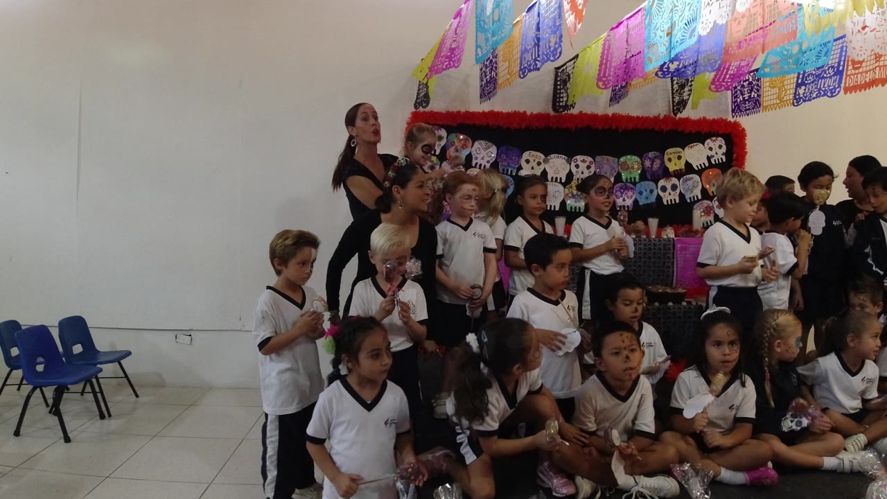Children seated and standing in Los Cabos, Mexico, face different directions as adults help arrange the group beneath hanging paper banners.