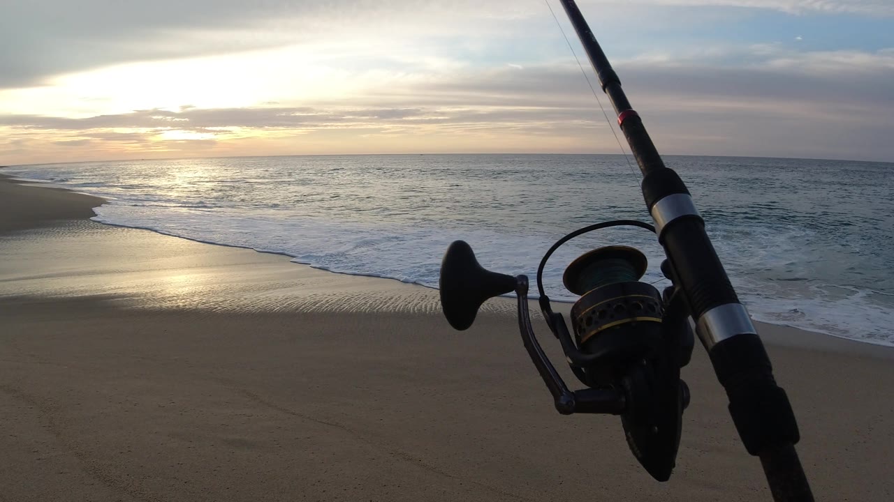 Fishing pole angled over surf and sunset water