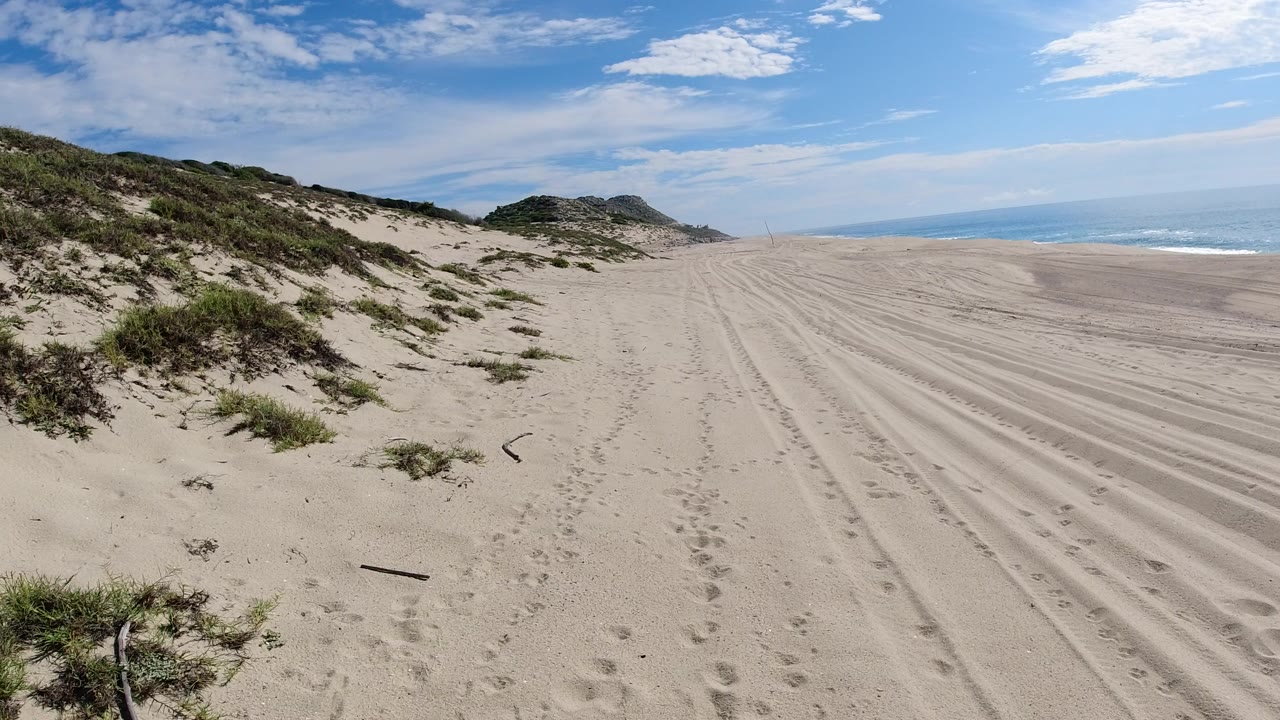 Sandy beach dunes with ocean at the right horizon.