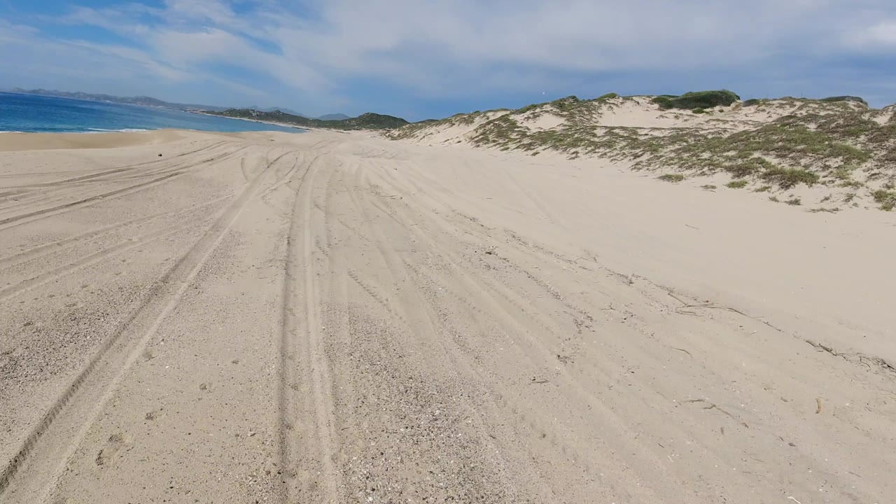 Rutted sand road curving between beach and dunes.