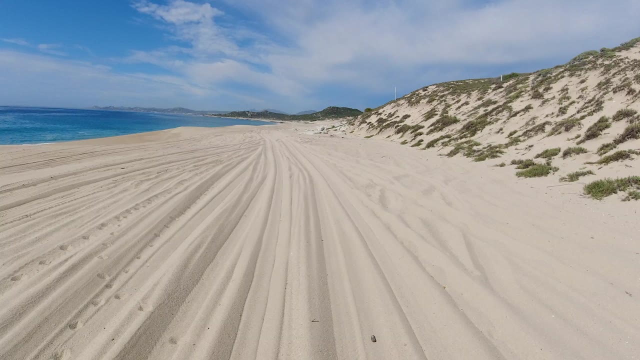 Wide sandy beach with ocean, dunes, tracks, and clouds