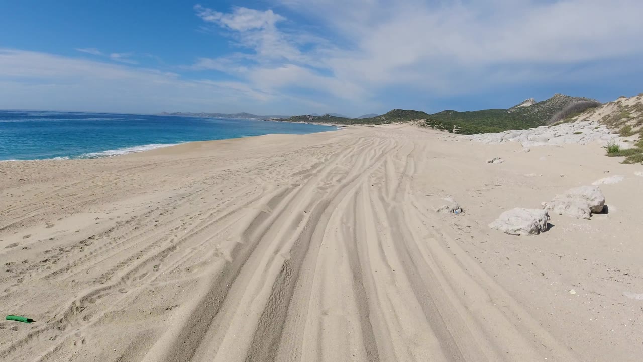 Beach tire tracks leading toward dunes and distant hills.