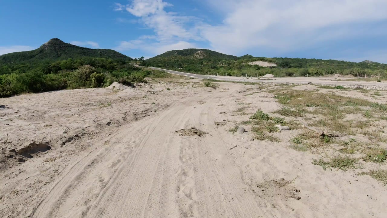 Sandy dirt path leading toward green hills under a blue sky.