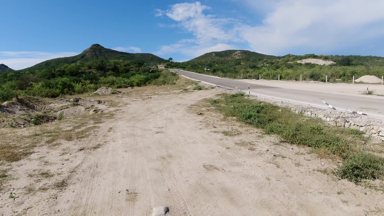 Open dirt pullout beside a quiet road and low mountains.