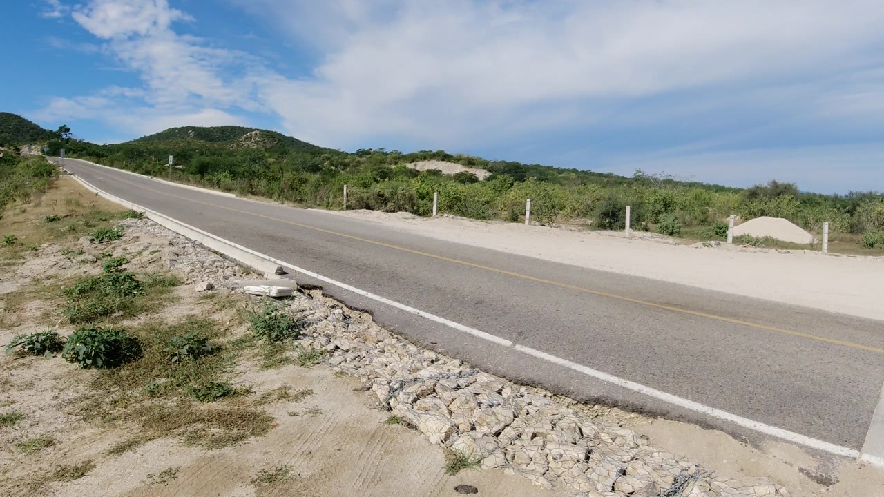 Road curve edge with scrub and hillside beyond
