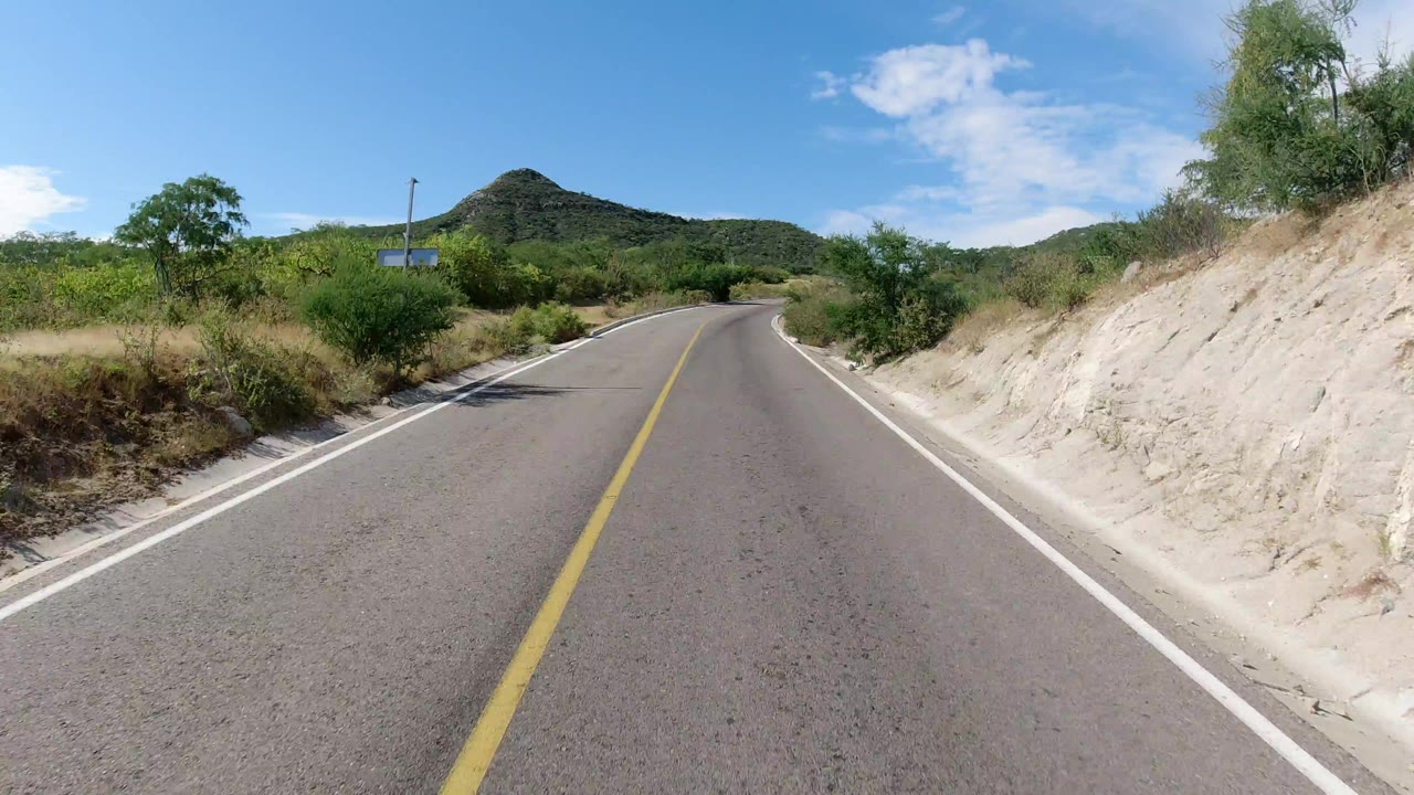 Paved road curving through sandy scrubland toward low hills.