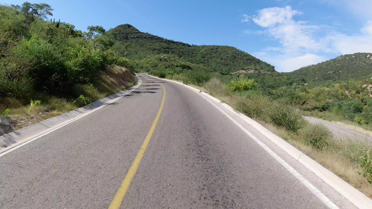 Curving mountain road bordered by green brush and low hills
