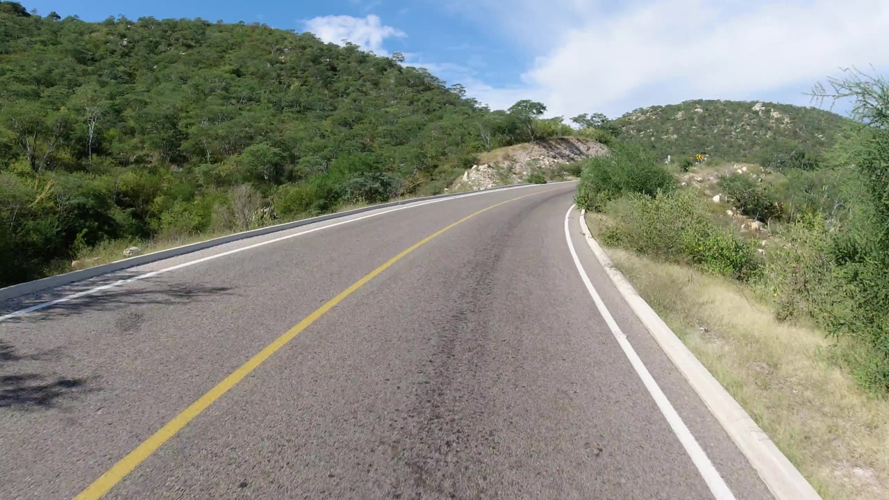 Road bending right past scrub and rocky hillside.