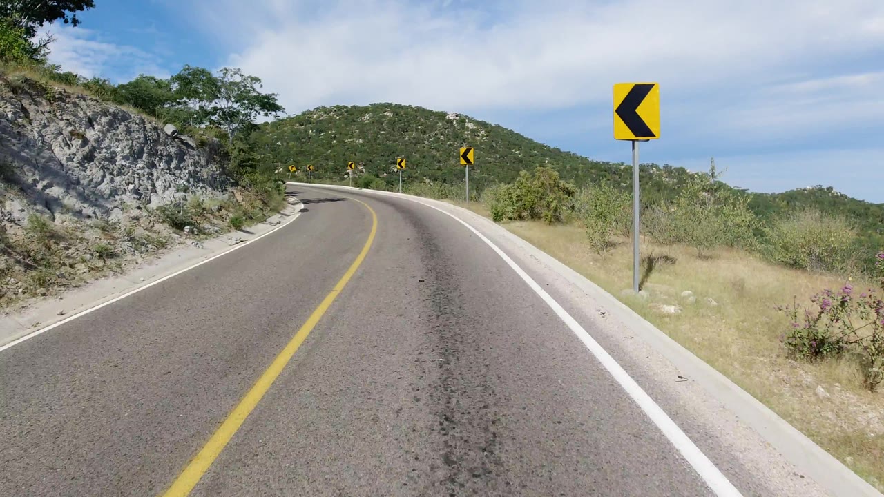Close roadside chevron sign beside a curving mountain road.