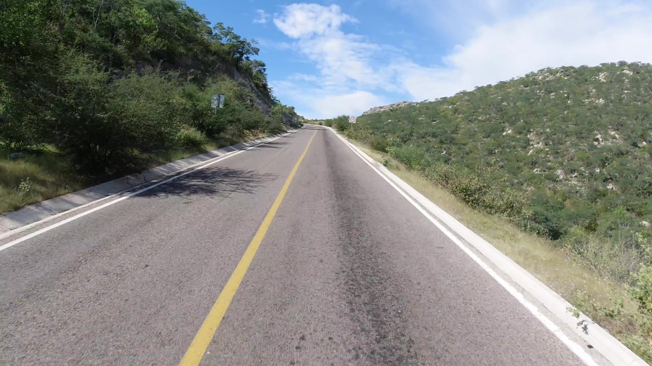 Empty highway curving beside brush and rocky hillside.