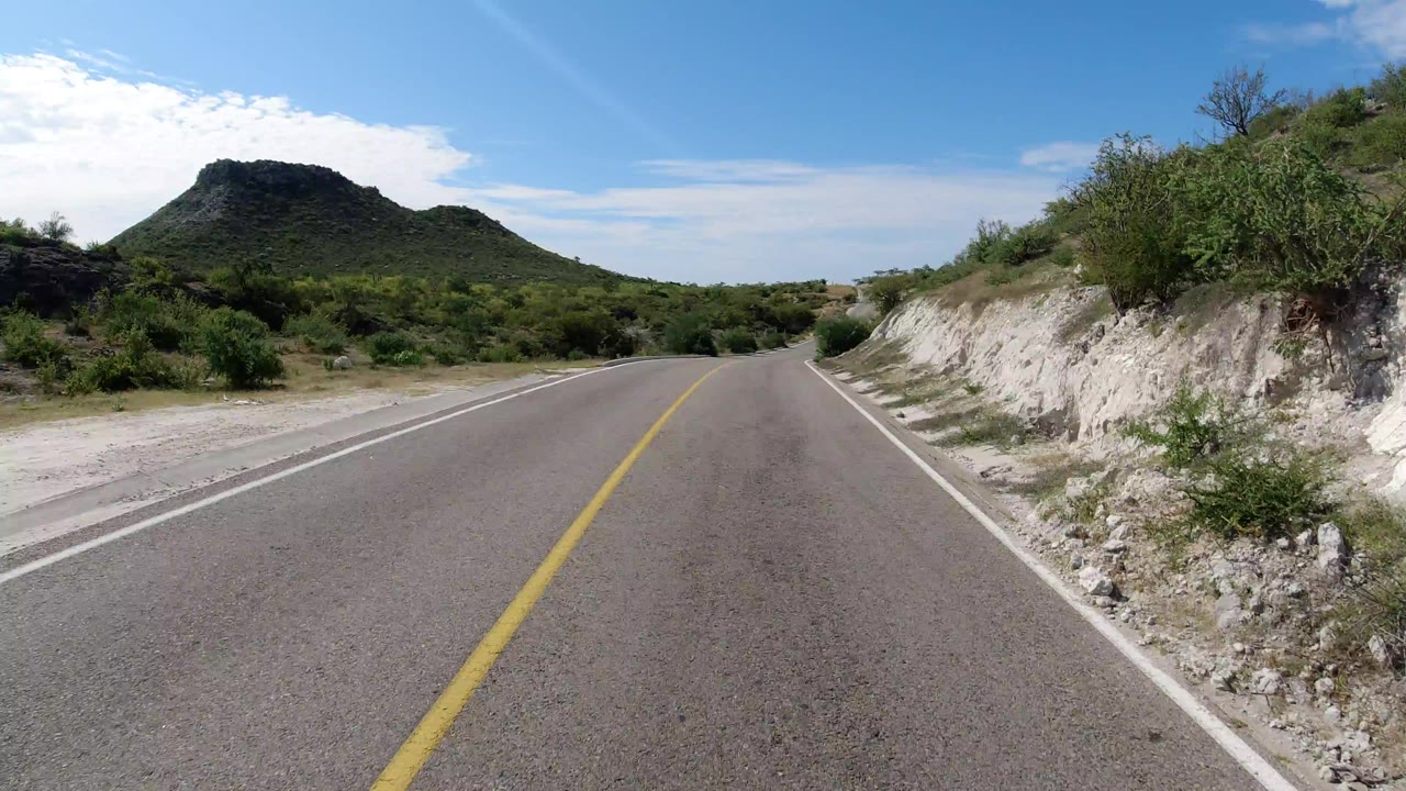 Two-lane road leading toward a low hill under blue sky