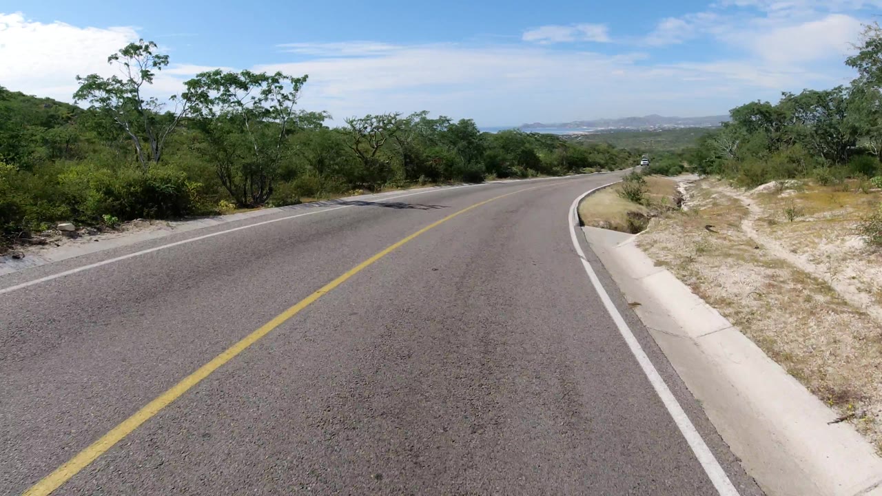 Paved road curving through dry vegetation with distant horizon.