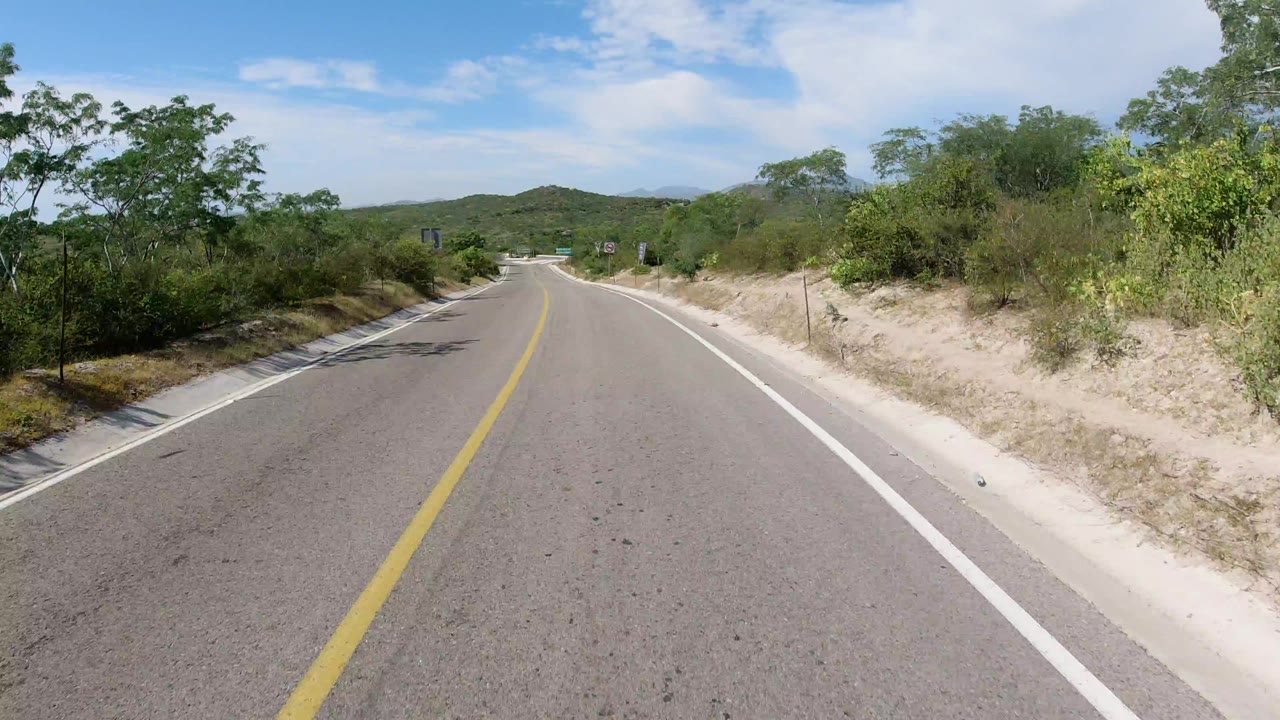 Paved road through dry green countryside under blue sky.