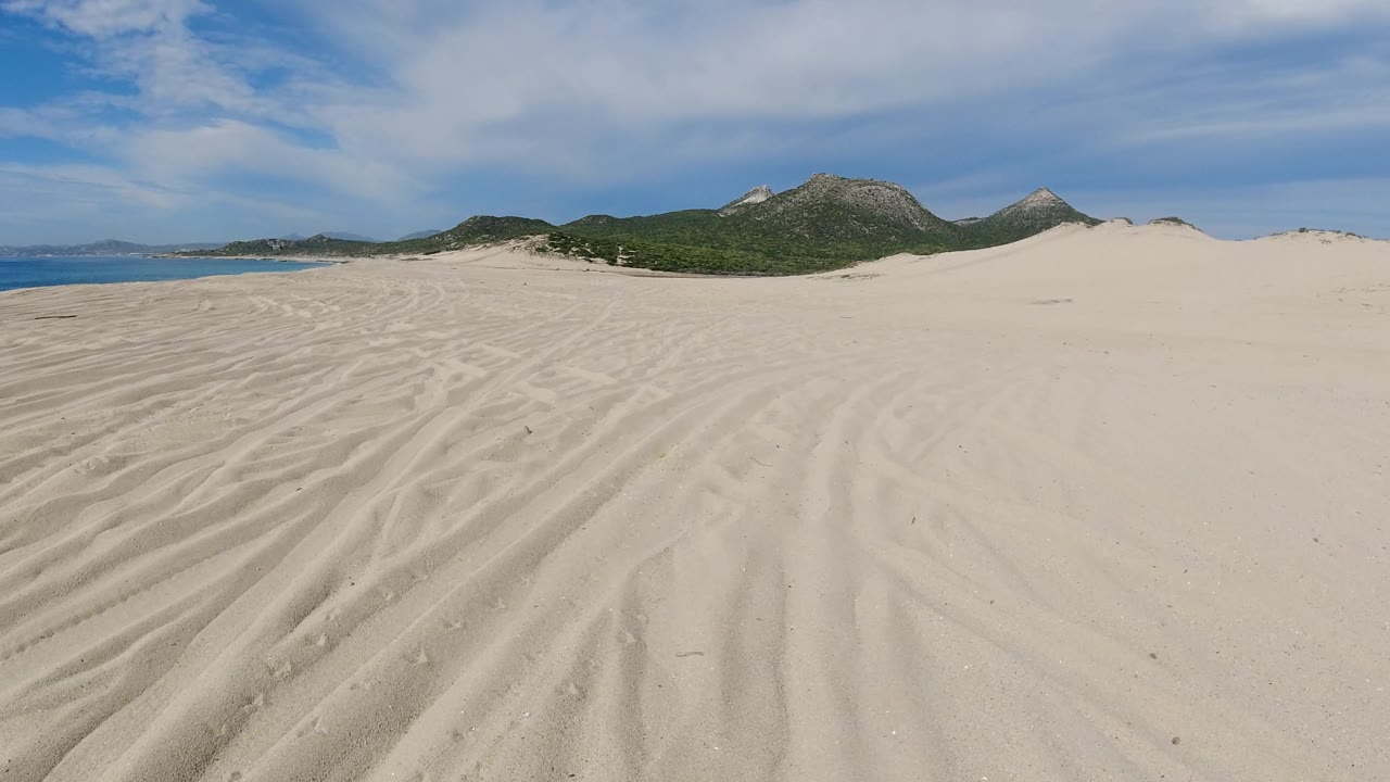 Open beach sand with coastal hills and dunes under clouds.