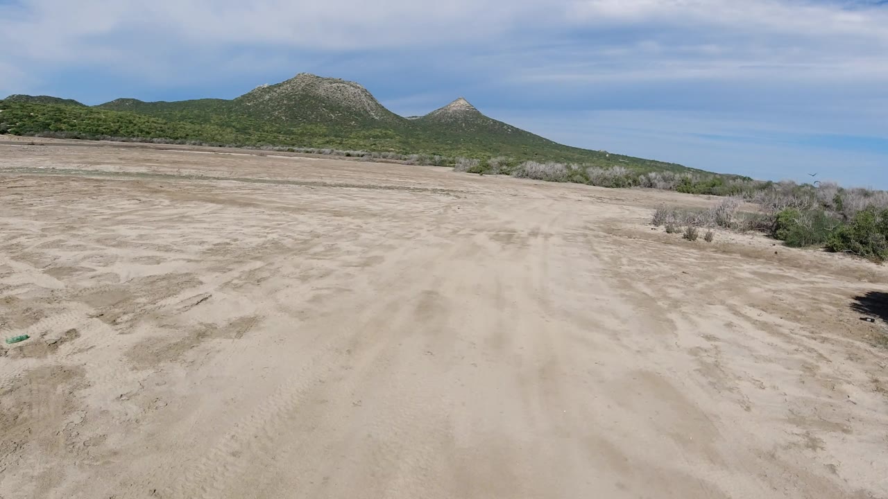Broad dirt path across scrubby desert terrain toward green hills.