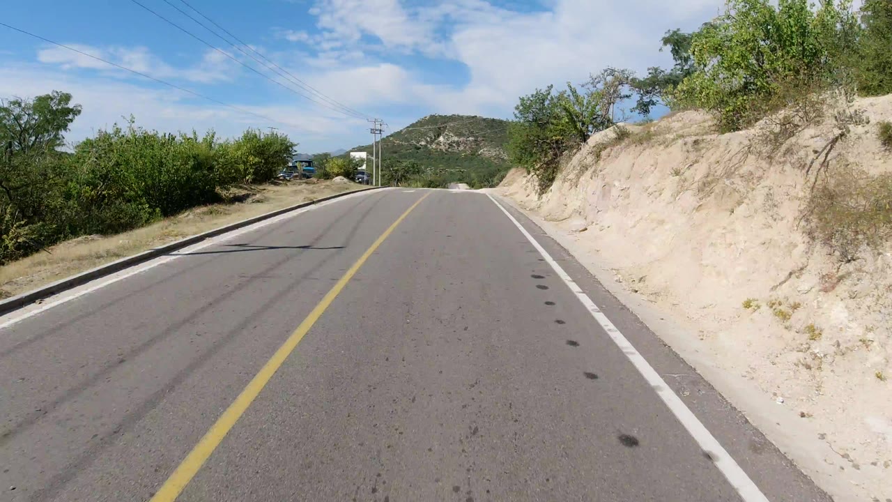 Two-lane road leading toward low hills under clouds.