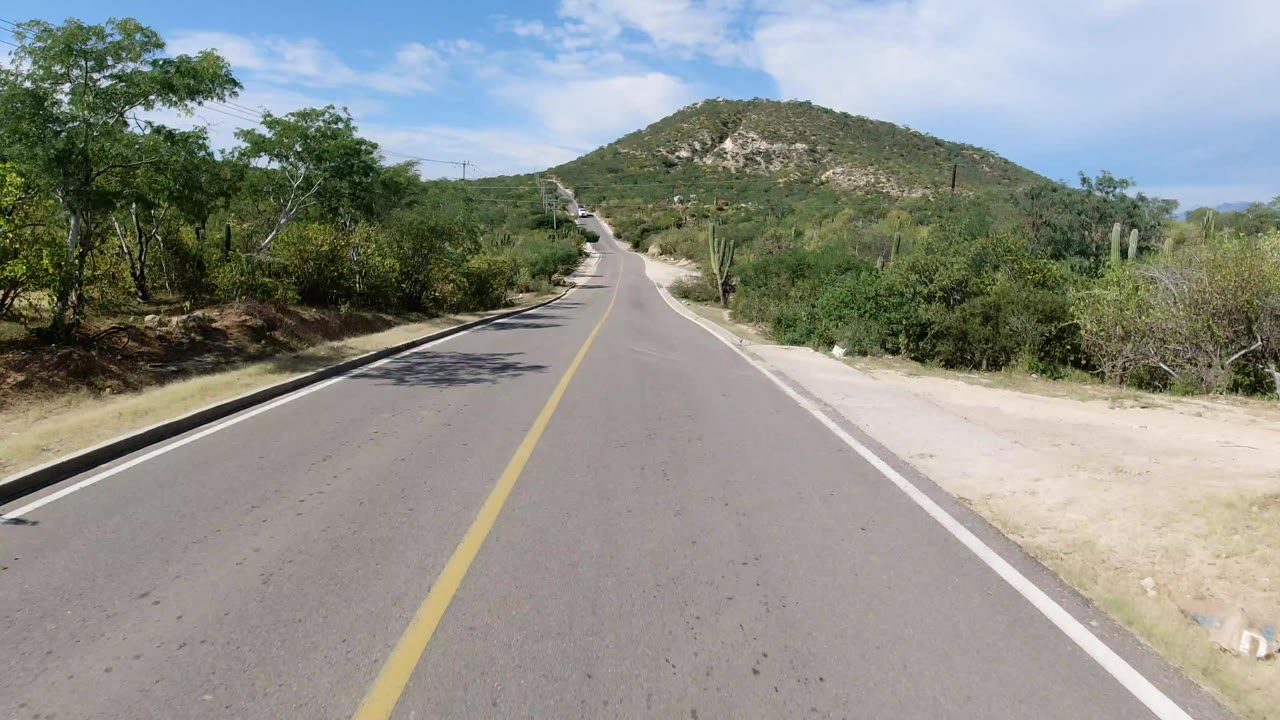 Two-lane desert road leading toward a green hill