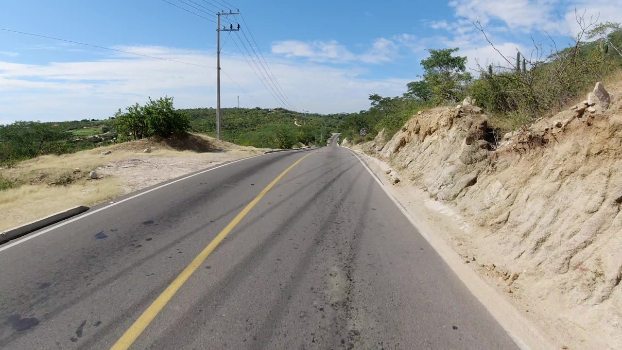 Curving paved road over a small rise with dry roadside brush