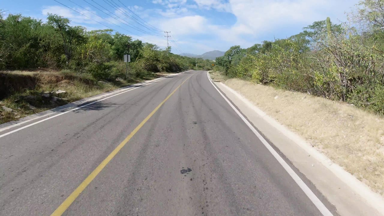 Road curving gently past dry brush and a small roadside sign.
