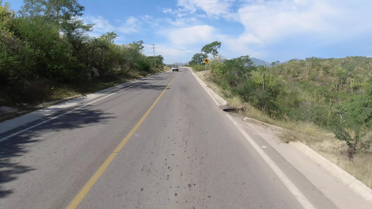 Paved road ahead with dry roadside vegetation and distant hills