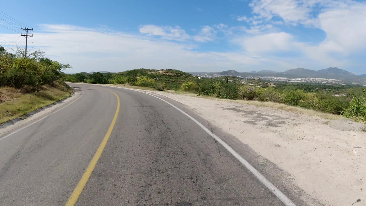 Empty road curve with roadside vegetation, utility pole, valley view, and hills.