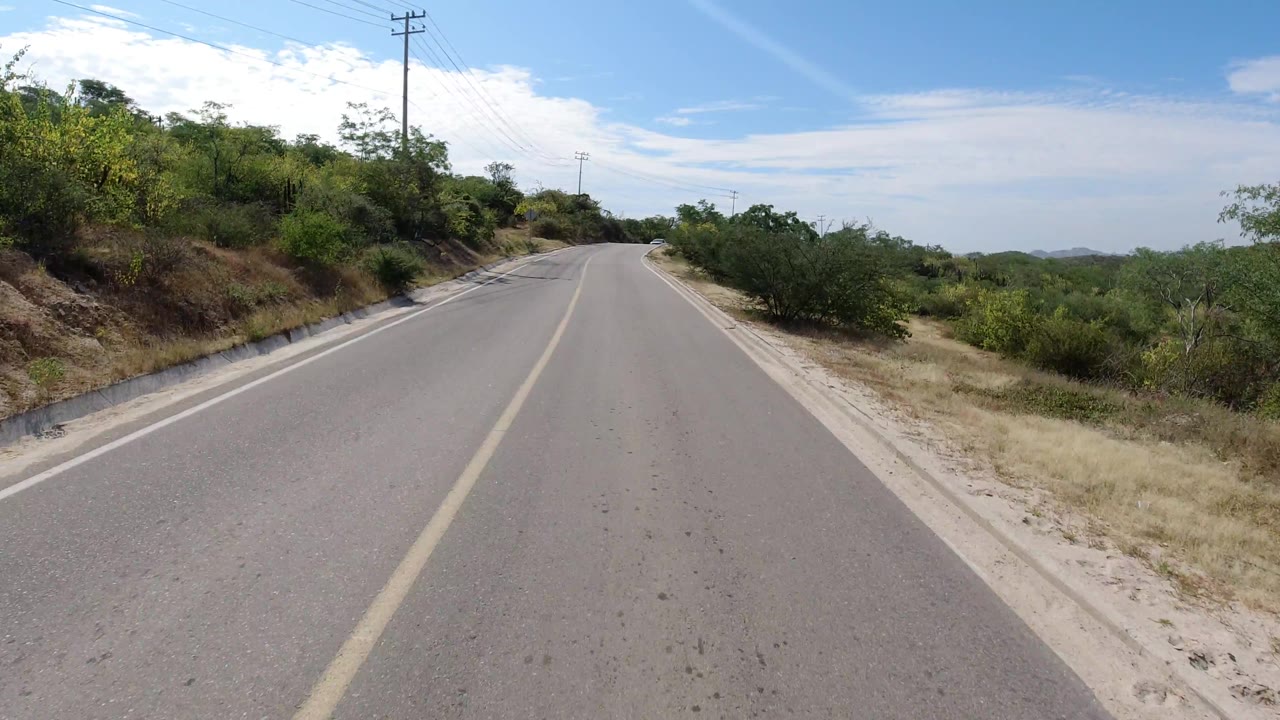 Open road stretching toward low hills with dry vegetation at the edges.