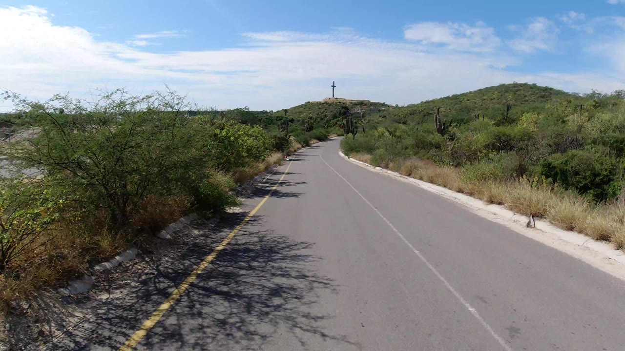 Paved road curving through desert brush under blue sky.