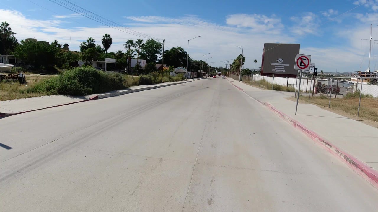 Wide paved road with sidewalks, signs, palms, and commercial buildings.