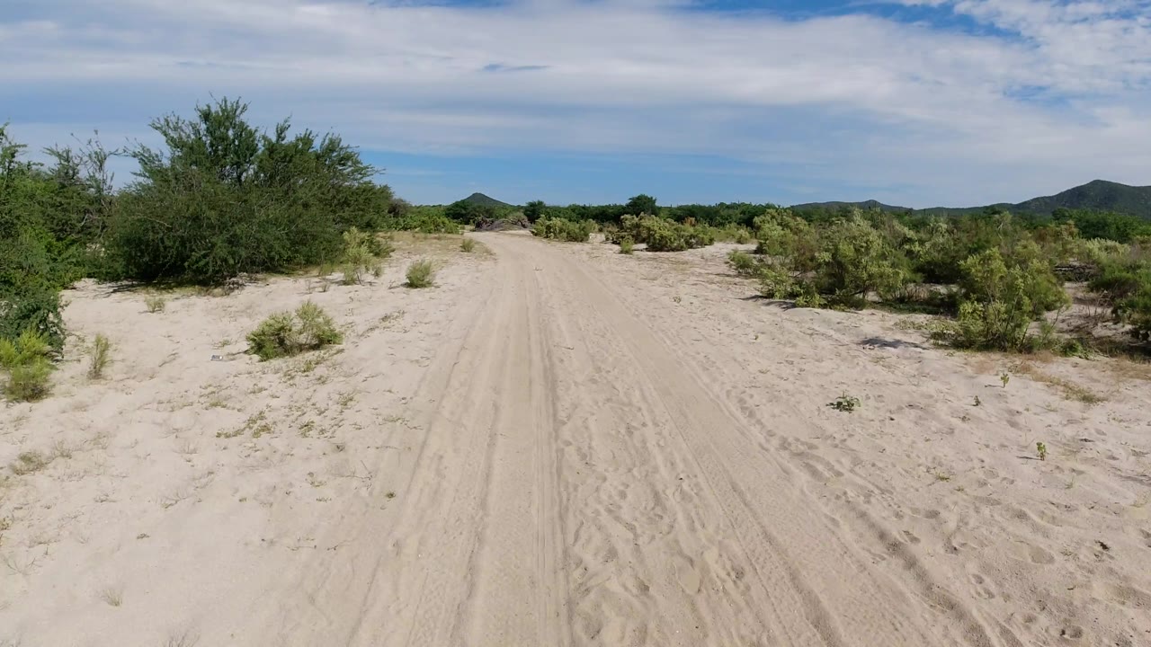 Wide sandy track with scrub on both sides and hills beyond.