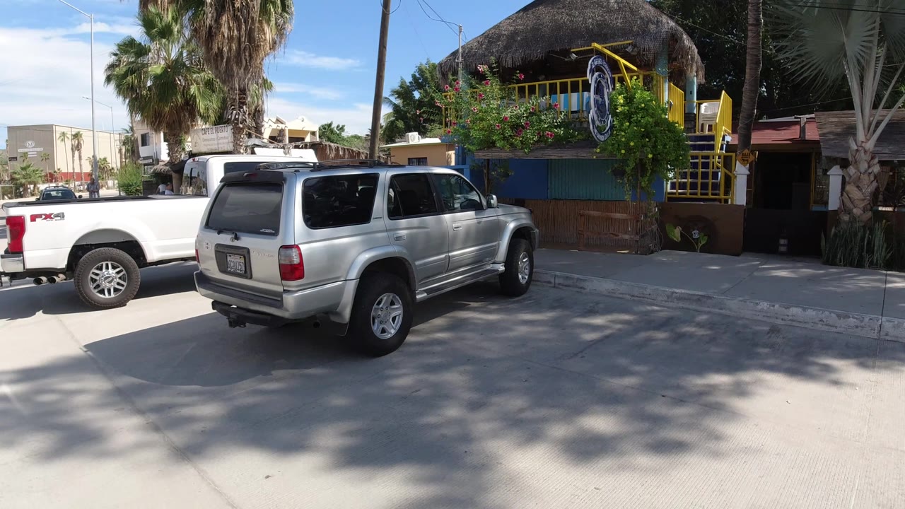 White pickup and silver SUV parked along a sunny street.
