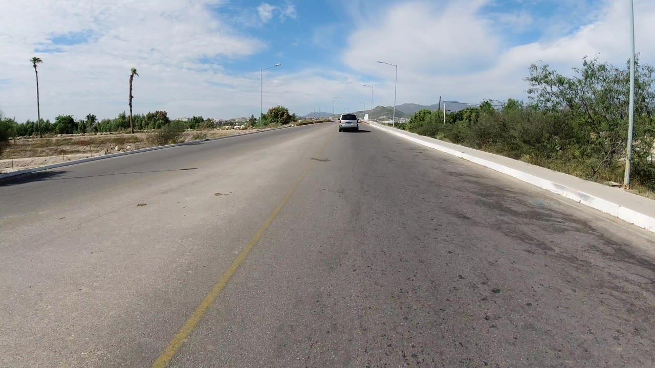 Wrangler on bridge-like road bordered by shrubs and low hills.