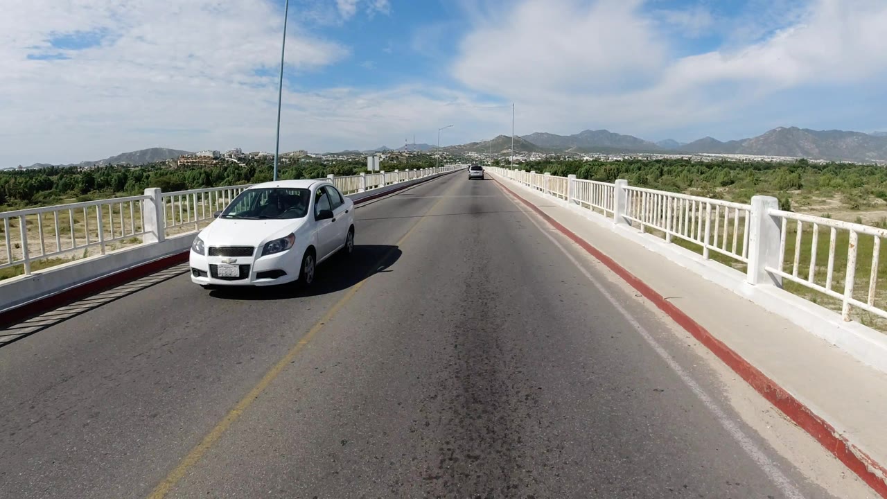 White car passing on a bridge road under bright sky
