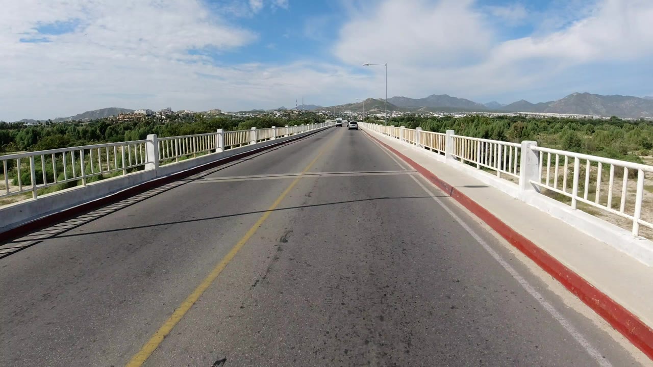 Bridge road with white railings, trees, hills, and blue sky