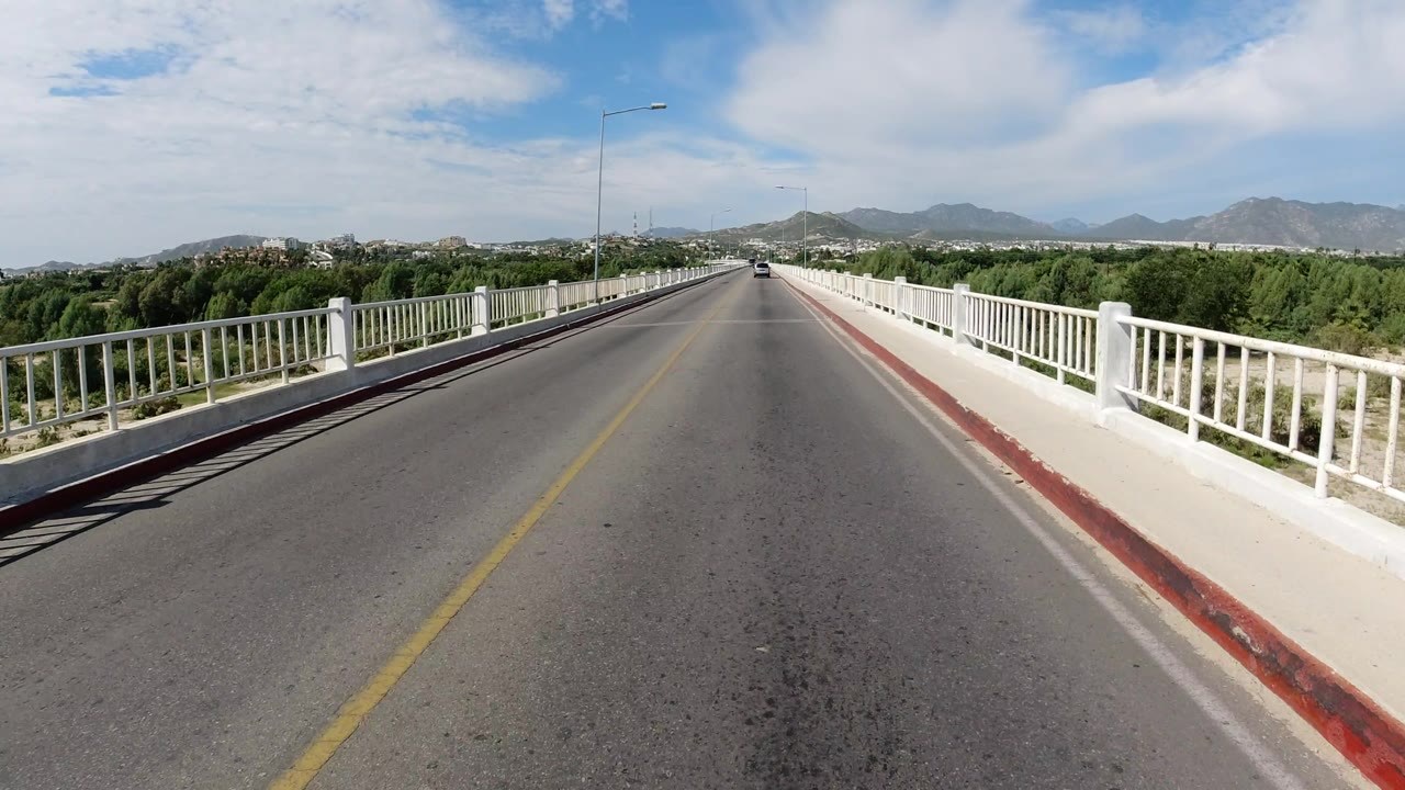 Open bridge road with trees on both sides and mountains ahead.