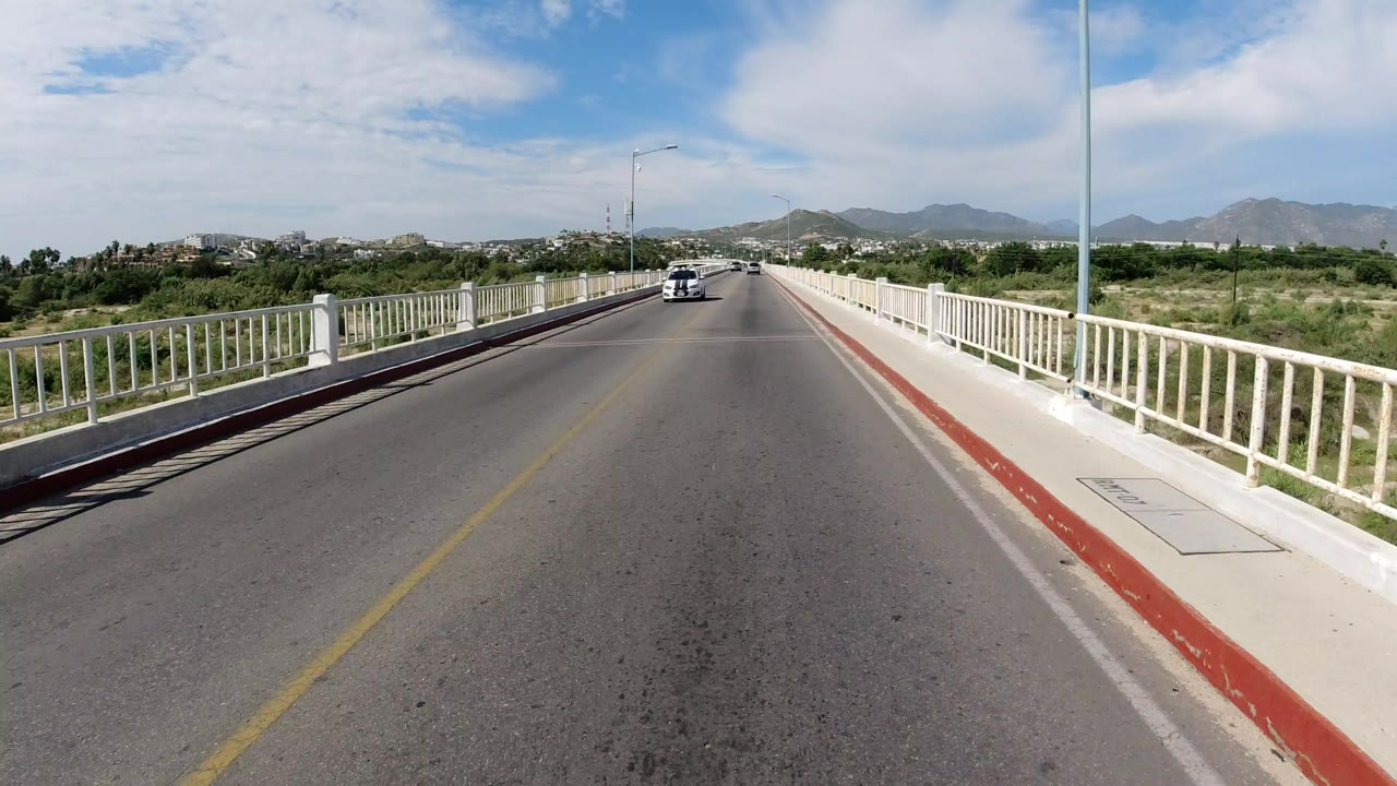 Forward view down a paved bridge with a white car in the distance.