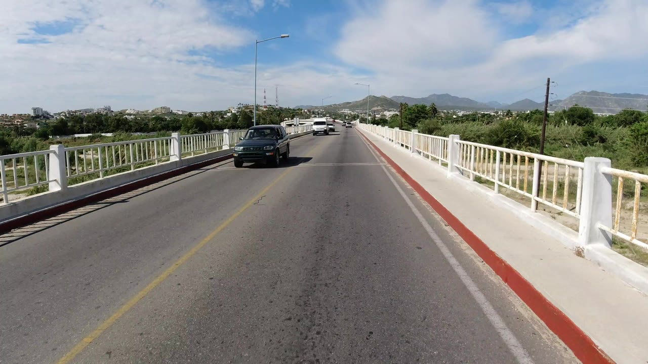 Bridge road with a dark car approaching under a bright sky.