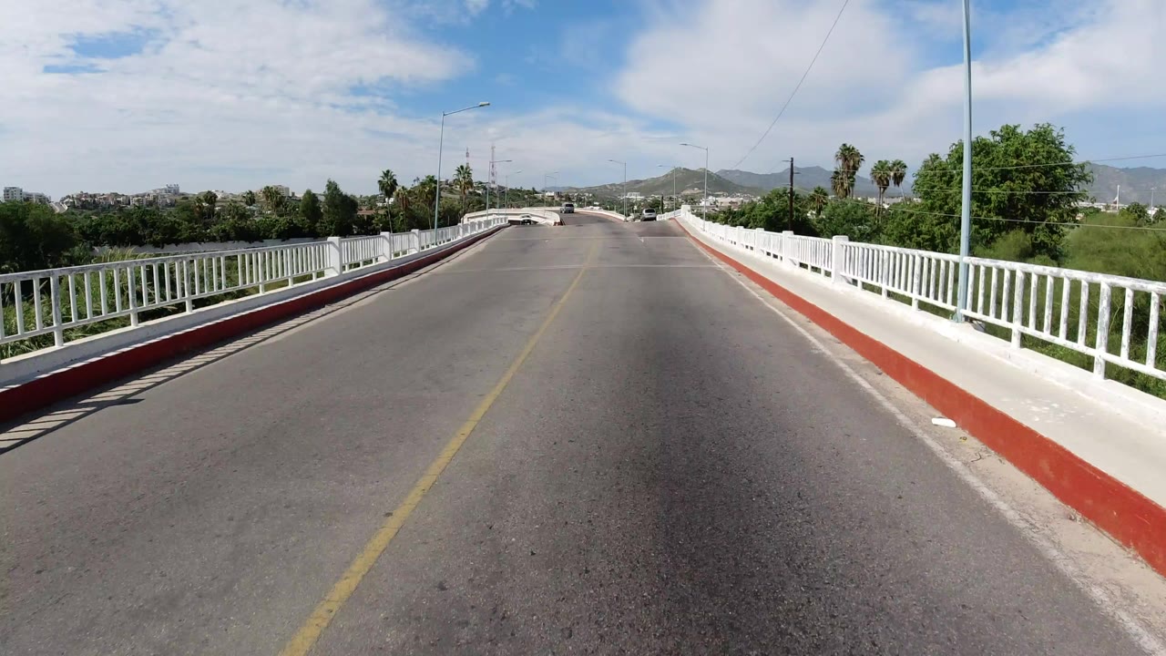 Empty bridge road with white railings and distant hills.