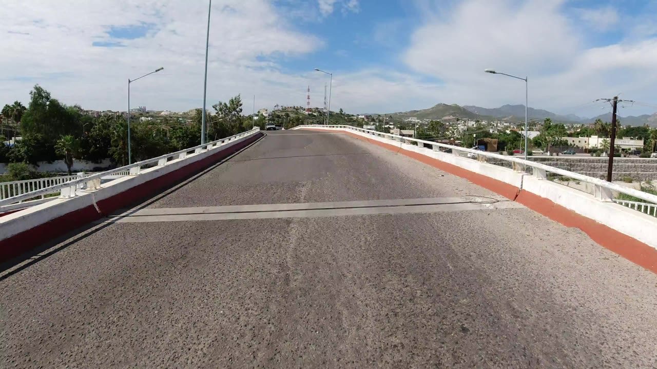 Empty paved road on a bridge with white guardrails and distant hills.