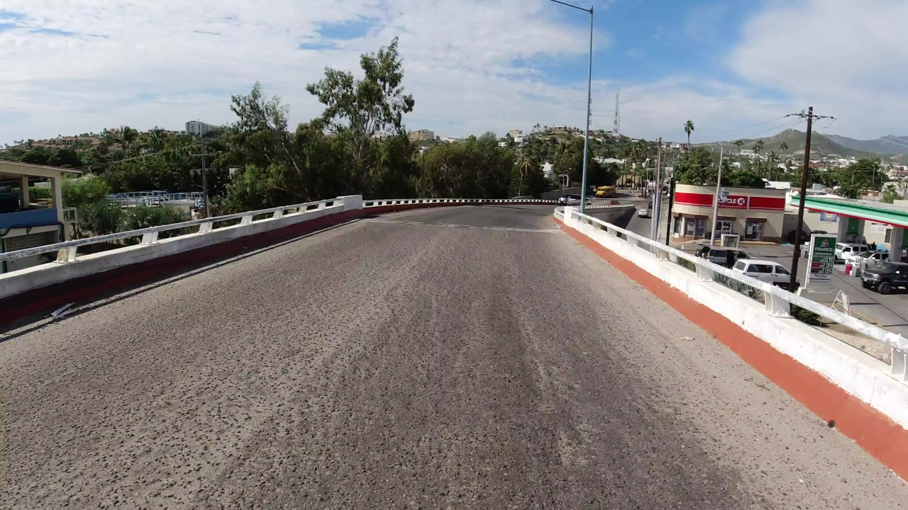 Elevated road with red-and-white rails, trees, low buildings, and distant hills.